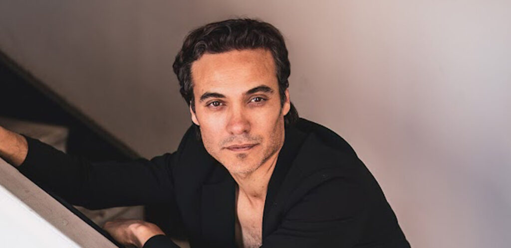 Argentinean actor, Martin Rodriguez from Netflix's GRISELDA mini-series, leaning over the staircase, wearing a black button-up shirt